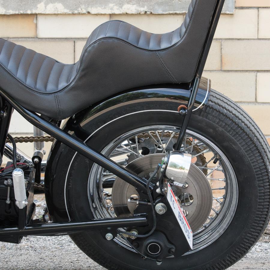 A black motorcycle with TC Bros Passenger Footpeg Kit for Sportster Hardtails by TC Bros. parked in front of a brick wall.