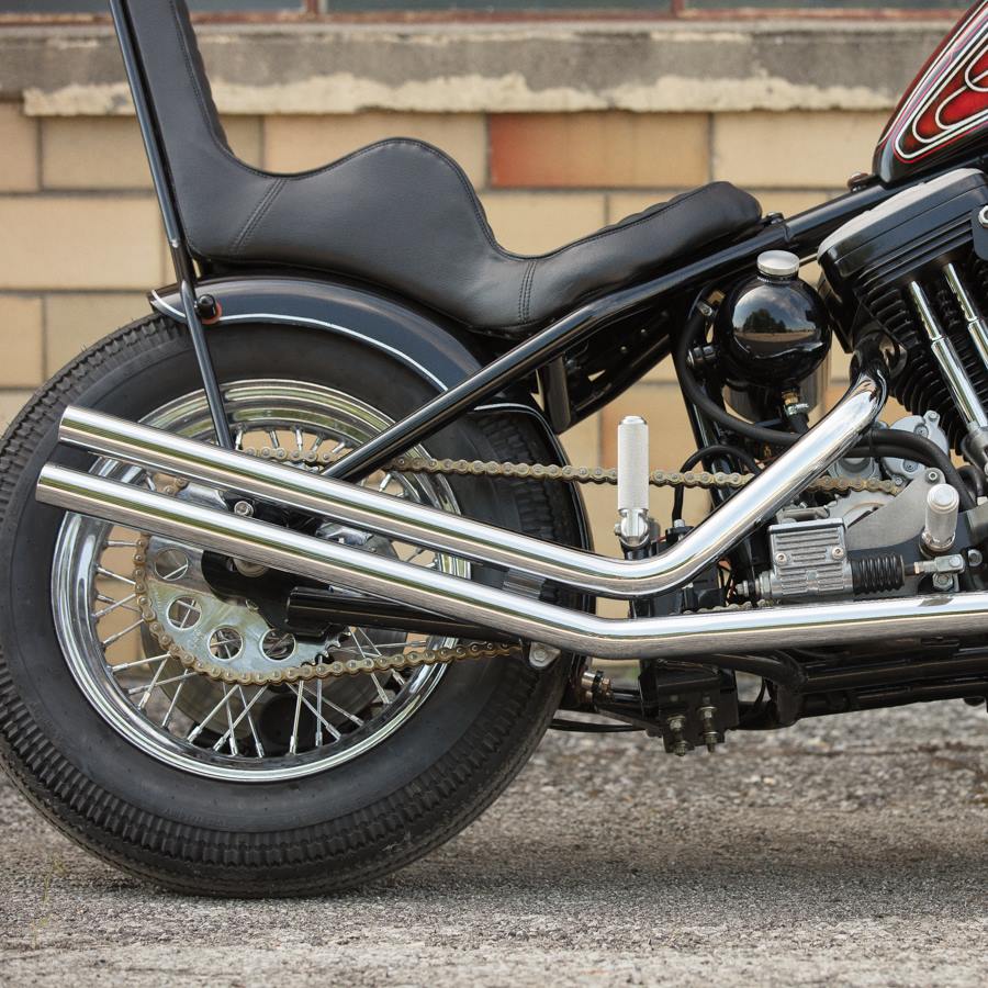 A TC Bros Passenger Footpeg Kit for Sportster Hardtails motorcycle parked in front of a brick wall.