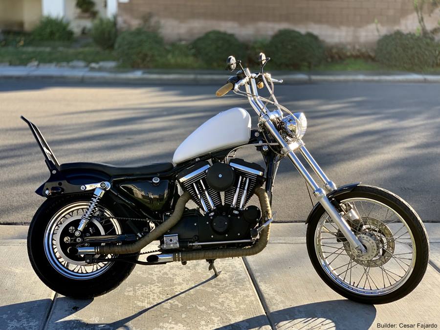 A TC Bros. Extended Fork Tube Kit +4" 39mm for Sportster/ Dyna Narrow Glide with a white and black Hard Chrome Finish is parked on the sidewalk.