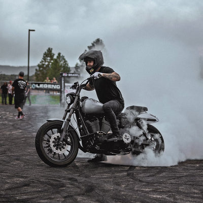 A man riding a motorcycle with smoke coming out of it. The motorcycle features TC Bros. 11.8in Profile™ Front Floating Brake Rotor for 2006-23 Harley Models on its front floating brake rotor, and the rider is cruising on one of the popular TC Bros. motorcycles.