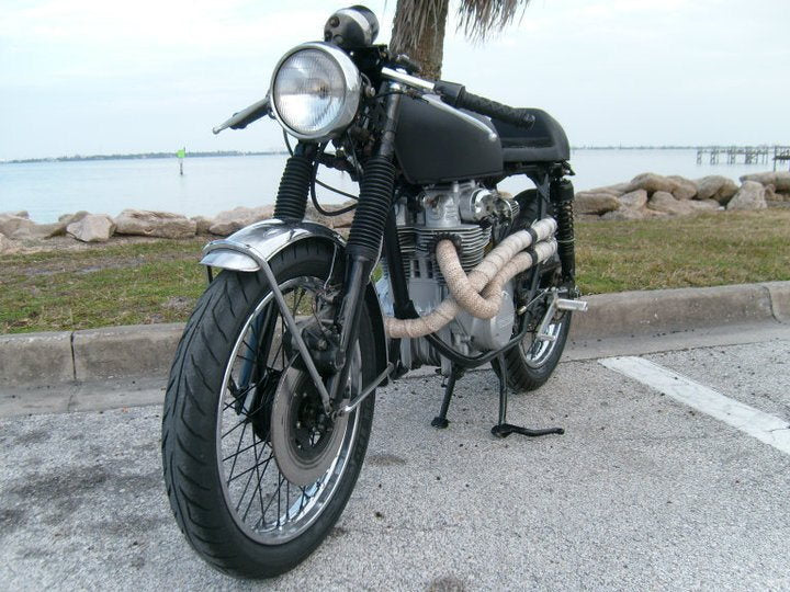A motorcycle with the Loaded Gun Custom Universal Rearsets by TC Bros. parked in front of a body of water.