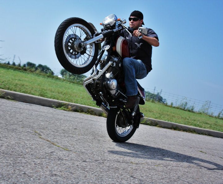 A man performing a trick on a motorcycle equipped with Loaded Gun Custom Universal Rearsets by TC Bros.
