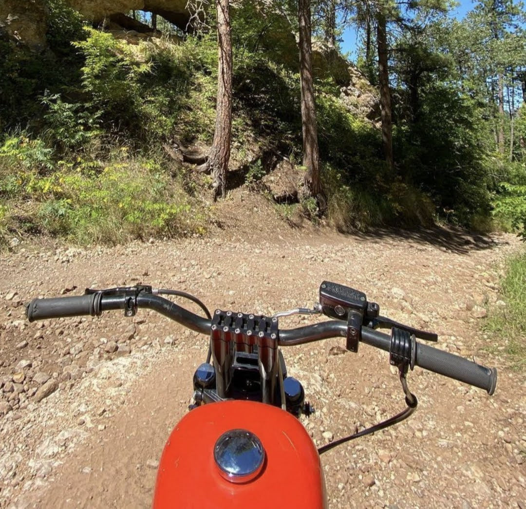 A TC Bros. Black motorcycle on a dirt road with trees in the background.
