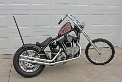 A black and silver motorcycle, featuring TC Bros. Sportster weld-on hardtails, parked in front of a garage.