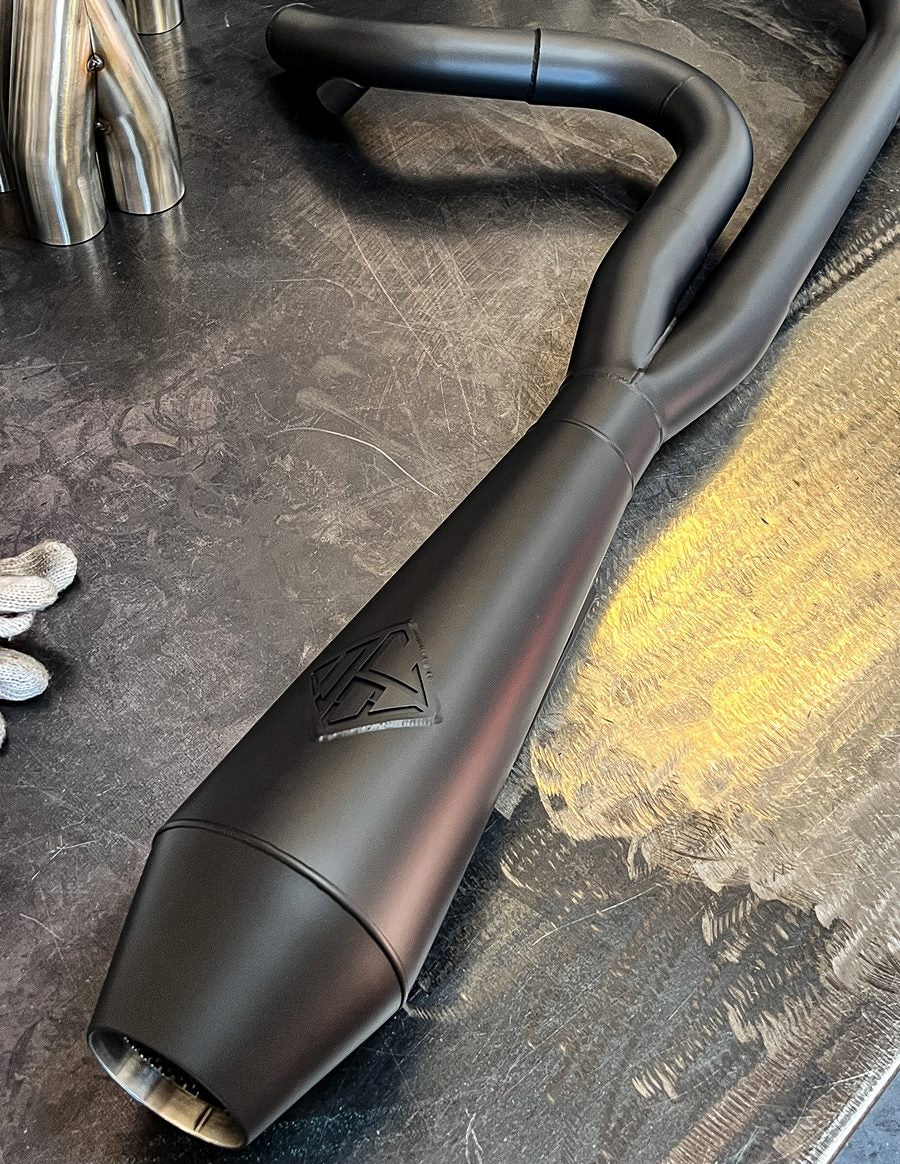A SP Concepts Big Bore Exhaust 06-17 Dyna (black) is sitting on a table.