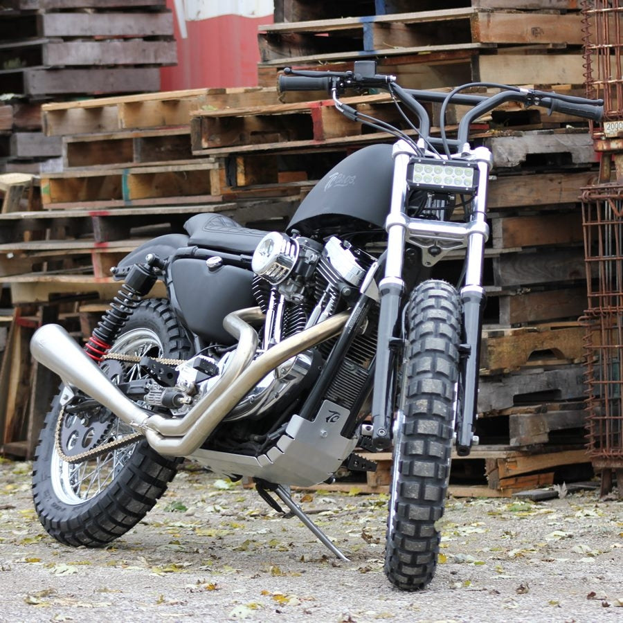 A motorcycle parked in front of pallets, featuring a Moto Iron® Chrome Rear Scrambler Wheel 40 spoke 18"x 2.5" Fits Sportster 1982-2003.