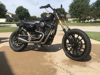 A TC Bros. Gold Titanium Nitride Coated Fork Tubes +2" Length 39mm for Sportster/ Dyna Narrow Glide motorcycle parked in front of a house.