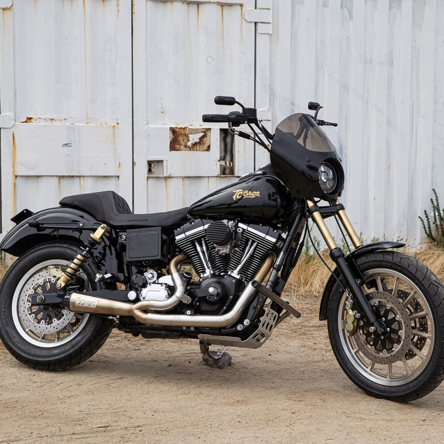 A black motorcycle parked in front of a barn with an aftermarket Saddlemen Step-Up Seat for 06-17 Dyna Models - Black Front Diamond Stitch.