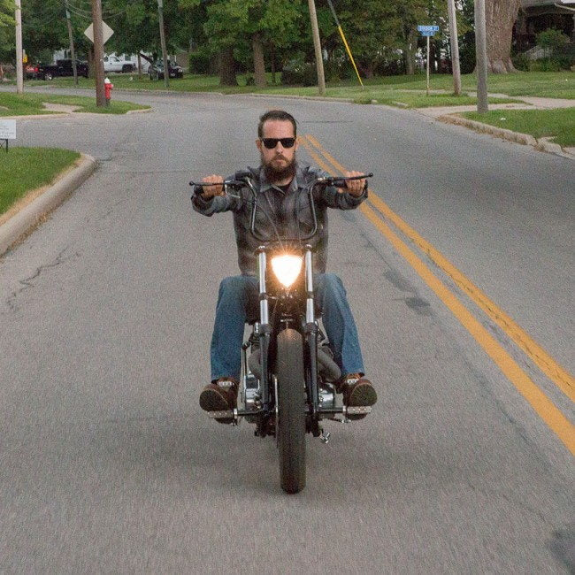 A man riding a motorcycle down a street with the Triangle Chopper Headlight - Aris Style -Chrome from Moto Iron® illuminating his way.