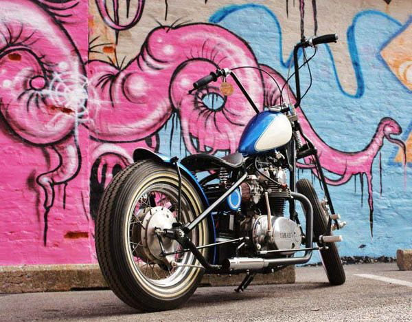 A TC Bros. motorcycle parked in front of a graffiti covered wall, showcasing the cool and edgy culture of TC Bros. choppers and bobbers.