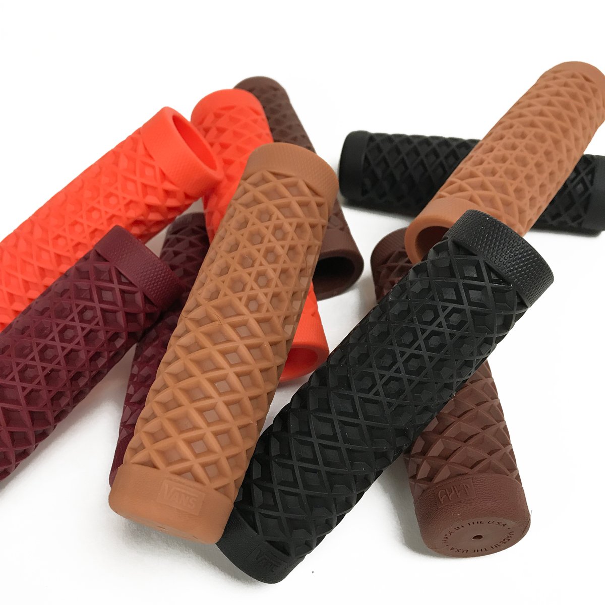 A group of different colored rubber grips, including the ODI Vans + Cult Motorcycle Grips - 7/8" Orange, on a white surface.