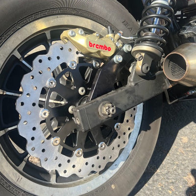 The TC Bros. 2000-2005 Harley Dyna Rear Axial Brembo Bracket Stock Rotor is a black bracket that comes with a bolt and nut. It is designed specifically for 2000-2005 Harley Dyna models.