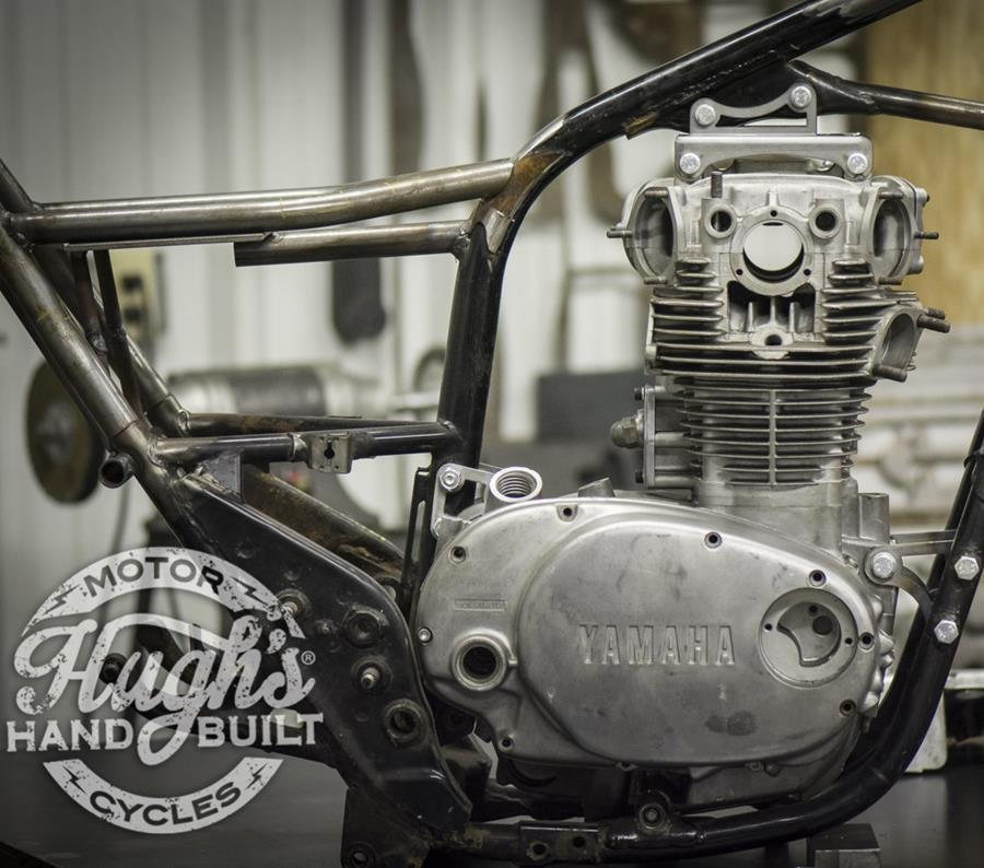 A picture of a motorcycle in a workshop, featuring the Hughs HandBuilt XS650 Top Motor Mount Window 1974-83 for the XS650, designed by Hughs Handbuilt.