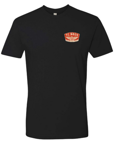 A TC Bros. Winged Wheel T-Shirt - Black made of ring-spun cotton with an orange logo.