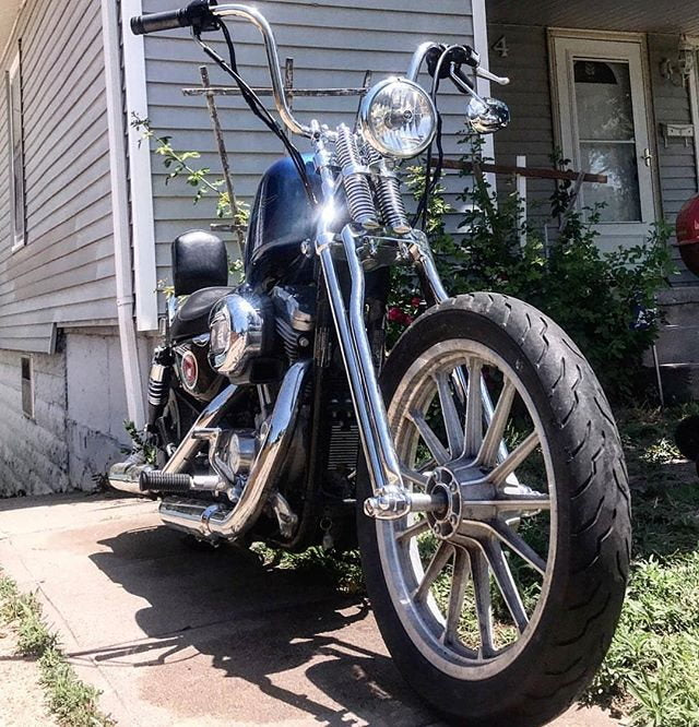 A Moto Iron® Wishbone Springer Front End motorcycle parked in front of a house.