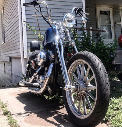 A motorcycle with a Moto Iron® Harley Wishbone Springer Front End parked in front of a house.