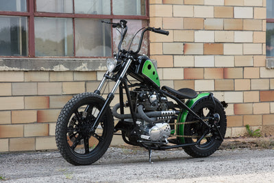 A green and black motorcycle parked in front of a brick building.