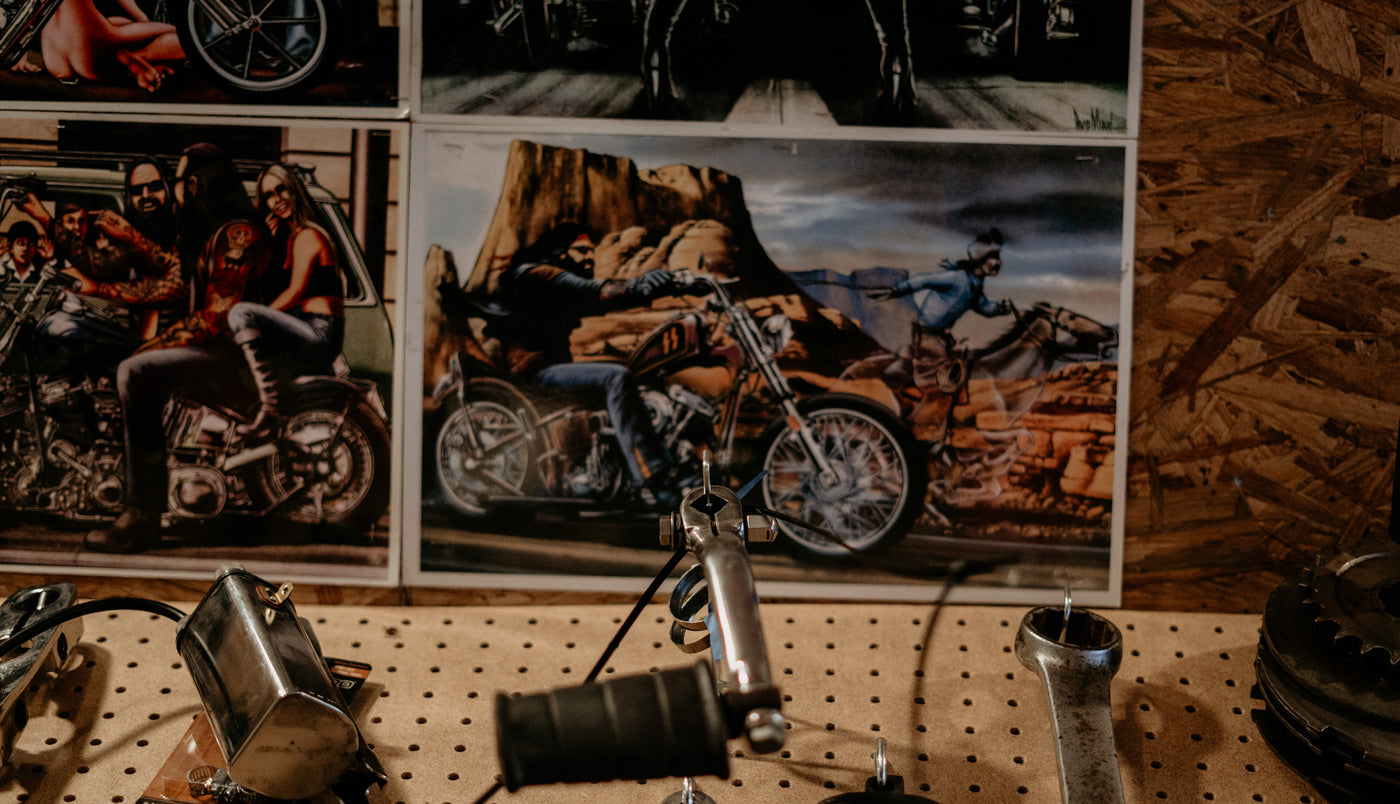 Posters of motorcycle riders are displayed on a wall above a wooden workbench with tools and motorcycle parts.