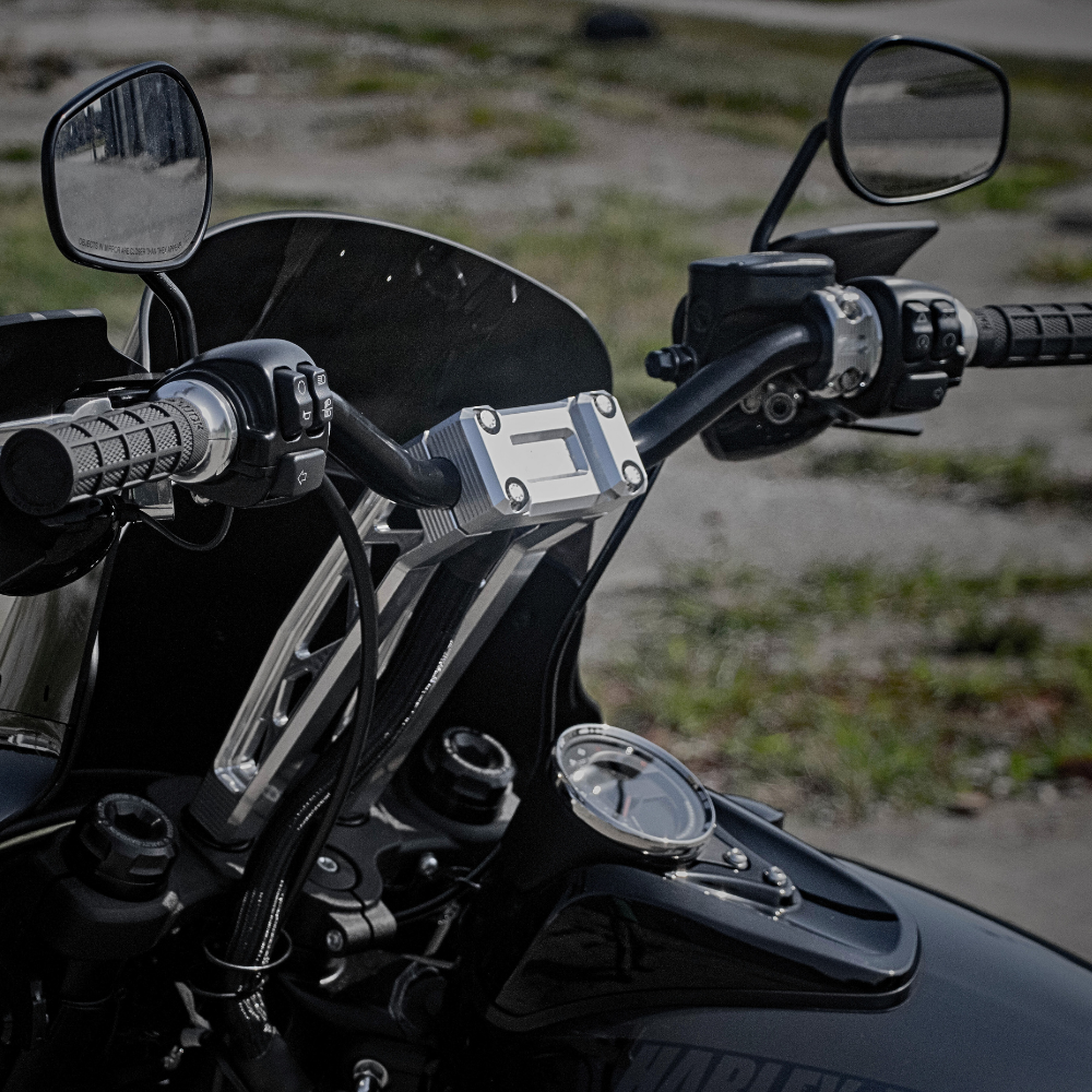 Close-up of the TC Bros. Pro Series Truss Pullback Riser for Harley-Davidson, featuring exposed bolts and cables against a blurred outdoor background. Crafted from billet aluminum, this TC Bros. riser offers rugged style and durability.