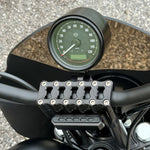 Two cylindrical motorcycle tachometer bezels from TC Bros., including the Pro Series 4 inch Gauge Relocation Bezel for Harley Davidson, in black and silver finishes with similar gauge faces featuring numbers and a red needle.