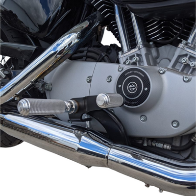 The TC Bros. Nomad Shift/Brake Peg for Harley-Davidson features CNC-machined aluminum pegs in silver, gold, and black with textured grips and threaded bolts. Ideal as a shift or brake peg. "NOMAD SHIFT/TOE PEG" text appears at the top.