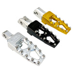 Three TC Bros. Pro Series MX Lite Foot Pegs for Harley Davidson models, featuring metallic spiked surfaces, are arranged side by side in silver, black, and gold.