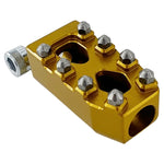 Close-up of a CNC-machined TC Bros. Pro Series MX Shifter/Brake Peg and foot peg assembly, mounted near the engine and exhaust pipes on a concrete surface.