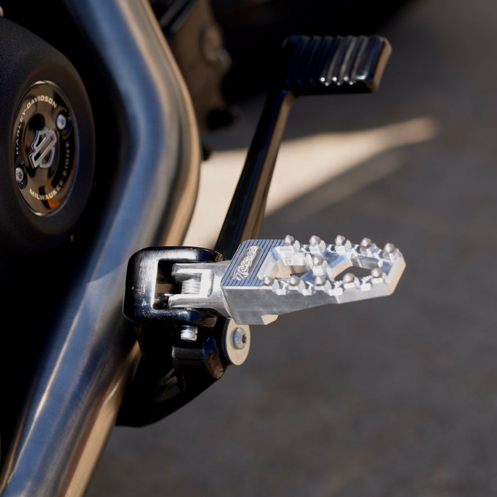 Three TC Bros. Pro Series MX Lite Foot Pegs for Harley Davidson models, featuring metallic spiked surfaces, are arranged side by side in silver, black, and gold.