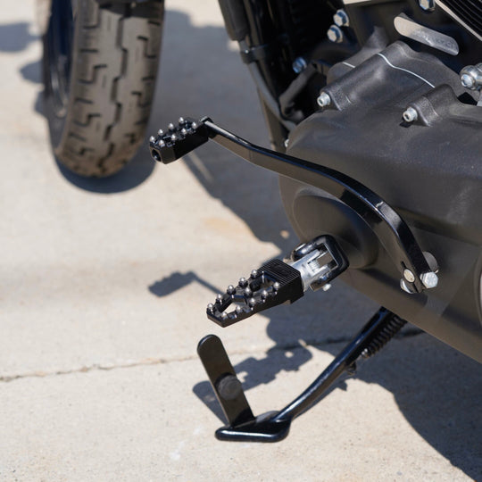 Three TC Bros. Pro Series MX Lite Foot Pegs for Harley Davidson models, featuring metallic spiked surfaces, are arranged side by side in silver, black, and gold.