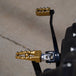 Three TC Bros. Pro Series MX Lite Foot Pegs for Harley Davidson models, featuring metallic spiked surfaces, are arranged side by side in silver, black, and gold.