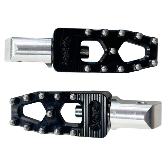 Two TC Bros. Pro Series Black MX Lite Passenger Foot Pegs for 2018-newer Harley Softail & Pan America with black, spiked foot platforms and silver attachment points, reminiscent of high performance motorcycle foot pegs, displayed side by side against a white background.