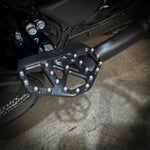 Three TC Bros. Pro Series MX Mini Floorboards for Harley-Davidson, in silver, black, and gold, are diagonally arranged on a white background.