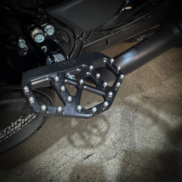 Three TC Bros. Pro Series MX Mini Floorboards for Harley-Davidson, in silver, black, and gold, are diagonally arranged on a white background.