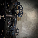 Three TC Bros. Pro Series MX Mini Floorboards for Harley-Davidson, in silver, black, and gold, are diagonally arranged on a white background.