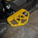 Three TC Bros. Pro Series MX Mini Floorboards for Harley-Davidson, in silver, black, and gold, are diagonally arranged on a white background.