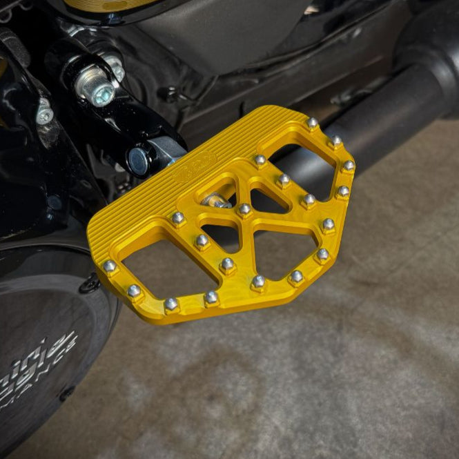 Three TC Bros. Pro Series MX Mini Floorboards for Harley-Davidson, in silver, black, and gold, are diagonally arranged on a white background.