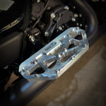 Close-up of a Harley-Davidson Bagger’s left side, featuring black bodywork, engine, and TC Bros. Pro Series MX Passenger Floorboards for 1993-Up Touring models with yellow metal accents on a concrete floor.