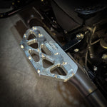 Close-up of a Harley-Davidson Bagger’s left side, featuring black bodywork, engine, and TC Bros. Pro Series MX Passenger Floorboards for 1993-Up Touring models with yellow metal accents on a concrete floor.