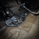 Close-up of a Harley-Davidson Bagger’s left side, featuring black bodywork, engine, and TC Bros. Pro Series MX Passenger Floorboards for 1993-Up Touring models with yellow metal accents on a concrete floor.