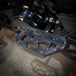 Close-up of a Harley-Davidson Bagger’s left side, featuring black bodywork, engine, and TC Bros. Pro Series MX Passenger Floorboards for 1993-Up Touring models with yellow metal accents on a concrete floor.