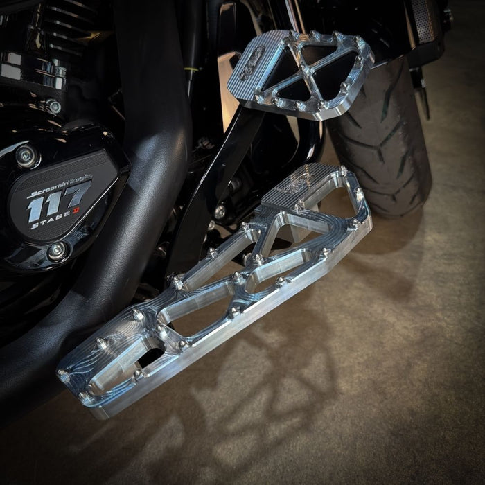 TC Bros. Pro Series MX Slim Floorboards for Harley Davidson Bagger Touring Models feature a skeletal design with metal pins, resembling high-performance pedals in silver, black, and gold. Arranged diagonally, they offer a striking visual appeal.