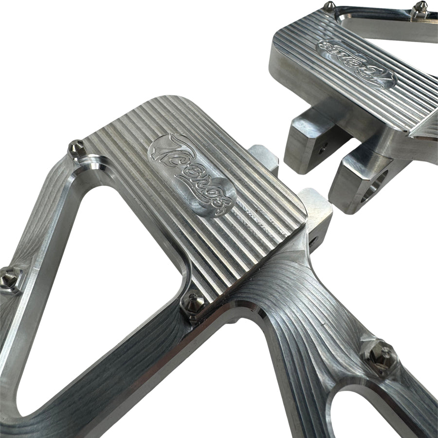 TC Bros. Pro Series MX Slim Floorboards for Harley Davidson Bagger Touring Models feature a skeletal design with metal pins, resembling high-performance pedals in silver, black, and gold. Arranged diagonally, they offer a striking visual appeal.