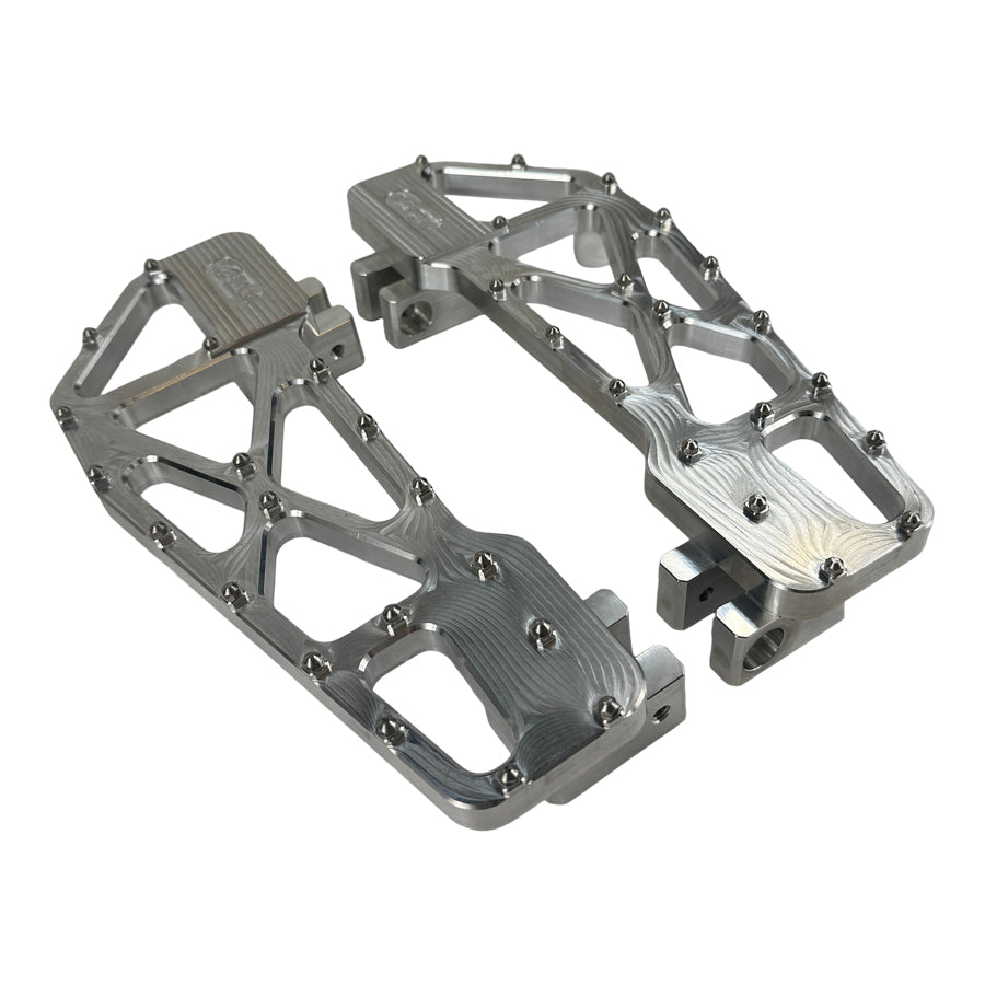 TC Bros. Pro Series MX Slim Floorboards for Harley Davidson Bagger Touring Models feature a skeletal design with metal pins, resembling high-performance pedals in silver, black, and gold. Arranged diagonally, they offer a striking visual appeal.