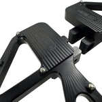 Close-up of TC Bros. Pro Series MX Slim Floorboards for 1984-Up Harley-Davidson Touring, featuring CNC-machined billet aluminum and visible bolts, mounted on a black Harley-Davidson motorcycle on a concrete floor.