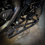 Close-up of TC Bros. Pro Series MX Slim Floorboards for 1984-Up Harley-Davidson Touring, featuring CNC-machined billet aluminum and visible bolts, mounted on a black Harley-Davidson motorcycle on a concrete floor.