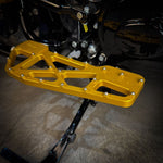 Close-up of TC Bros. Pro Series MX Slim Floorboards for 1984-Up Harley-Davidson Touring, featuring CNC-machined billet aluminum and visible bolts, mounted on a black Harley-Davidson motorcycle on a concrete floor.