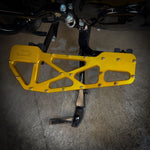 Close-up of TC Bros. Pro Series MX Slim Floorboards for 1984-Up Harley-Davidson Touring, featuring CNC-machined billet aluminum and visible bolts, mounted on a black Harley-Davidson motorcycle on a concrete floor.