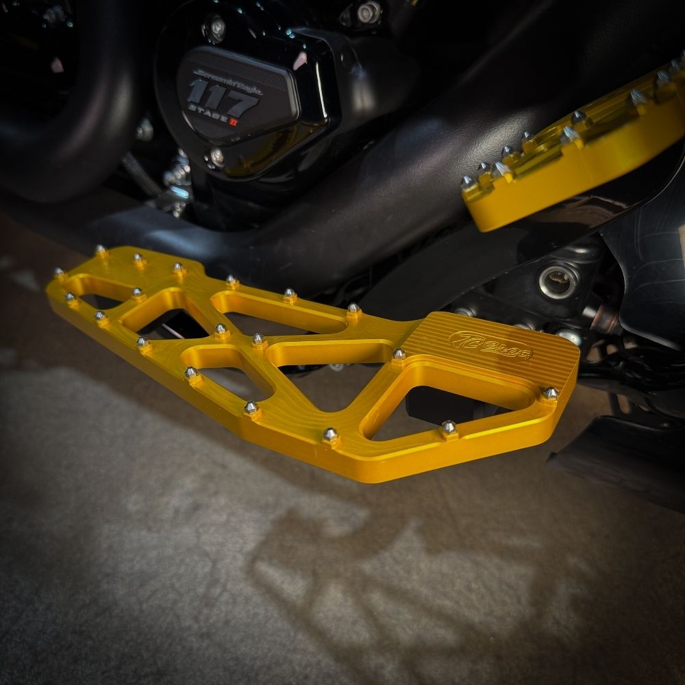 TC Bros. Pro Series MX Slim Floorboards for Harley Davidson Bagger Touring Models feature a skeletal design with metal pins, resembling high-performance pedals in silver, black, and gold. Arranged diagonally, they offer a striking visual appeal.