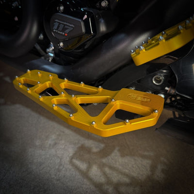 TC Bros. Pro Series MX Slim Floorboards for Harley Davidson Bagger Touring Models feature a skeletal design with metal pins, resembling high-performance pedals in silver, black, and gold. Arranged diagonally, they offer a striking visual appeal.