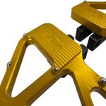 Close-up of TC Bros. Pro Series MX Slim Floorboards for 1984-Up Harley-Davidson Touring, featuring CNC-machined billet aluminum and visible bolts, mounted on a black Harley-Davidson motorcycle on a concrete floor.